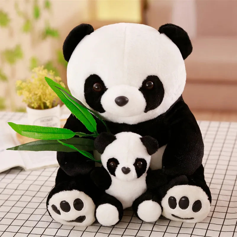 Two panda plush toys with a smaller one holding a leaf on a checkered surface.
